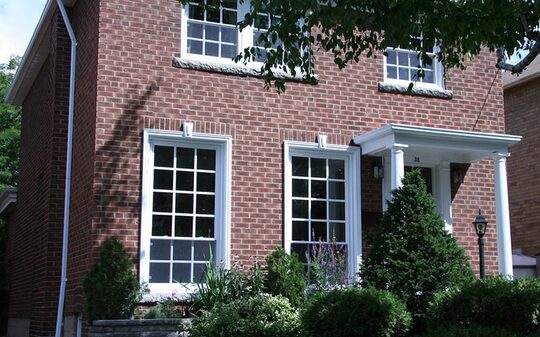Front house view of a red brick house with whites pillars and sliding windows